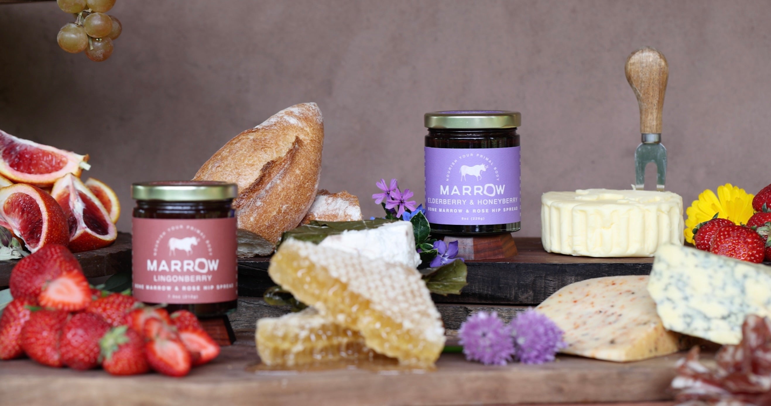 Marrow products including jars, honeycomb, and fruits on a wooden board with a neutral background.